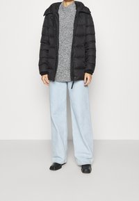 Svart puffjacka med huva, grå stickad tröja, ljusblå vida jeans och svarta skor. Slät textur, avslappnad design, funktionell stil.