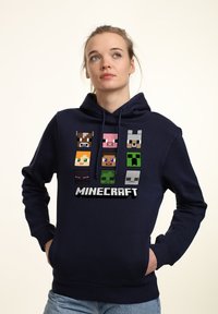 Felpa blu navy con cappuccio caratterizzata da personaggi pixelati di Minecraft stampati sulla parte anteriore. Realizzata in tessuto morbido, con cappuccio regolabile tramite cordoncino e tasca a marsupio.