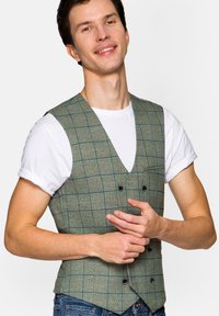 Zielona kamizelka w kratę, wykonana z teksturowanej tkaniny, z dekoltem w kształcie litery V, zdobiona podwójnymi guzikami i dwoma czarnymi guzikami, noszona na białej koszulce.
