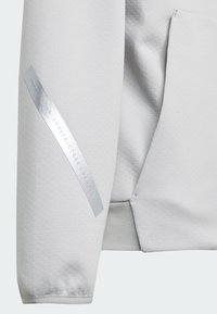 Sweatshirt gris clair présentant un tissu texturé et une étiquette argent métallique sur la manche avec le texte "CHAMPIONS DES CONSTRUCTEURS DE FORMULA ONE".