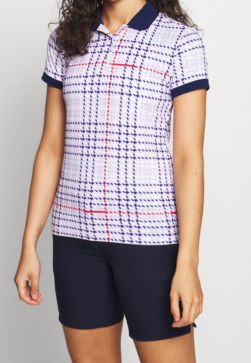 Vit polo shirt med marinblå krage, med ett rutmönster i blått och röd, kombinerat med figursydda marinblå shorts. Korta ärmar med definierade manschetter.