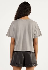 Szary krótki t-shirt z krótkimi rękawami, surowymi brzegami i miękką teksturą. W połączeniu z czarnymi skórzanymi szortami z podwiniętym dołem.