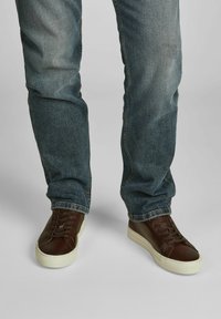 Bruine leren sneakers met een witte rubberen zool, voorzien van vlakke veters en een gladde afwerking, gedragen met blauwe spijkerjeans.