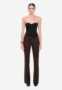 Schwarzer trägerloser Bodysuit mit gepolsterten Cups, kombiniert mit dunkelbraunen Wildleder-Flare-Hosen mit Schnürdetail am Bund und flachen Schuhen.