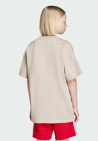 Beige tričko s krátkymi rukávmi a voľným strihom, s okrúhlym výstrihom a hladkým povrchom, doplnené červenými šortkami so bočnými pruhmi.