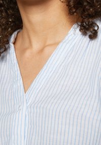 Jasnoniebieska i biała tkanina w paski z dekoltem w serek i miękką teksturą, prezentująca cienkie pionowe linie oraz luźny fason.