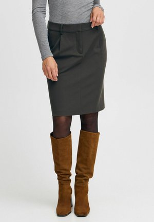 Jupe crayon gris foncé avec plis sur le devant, associée à des bottes hautes en daim marron. Le tissu semble lisse et structuré.