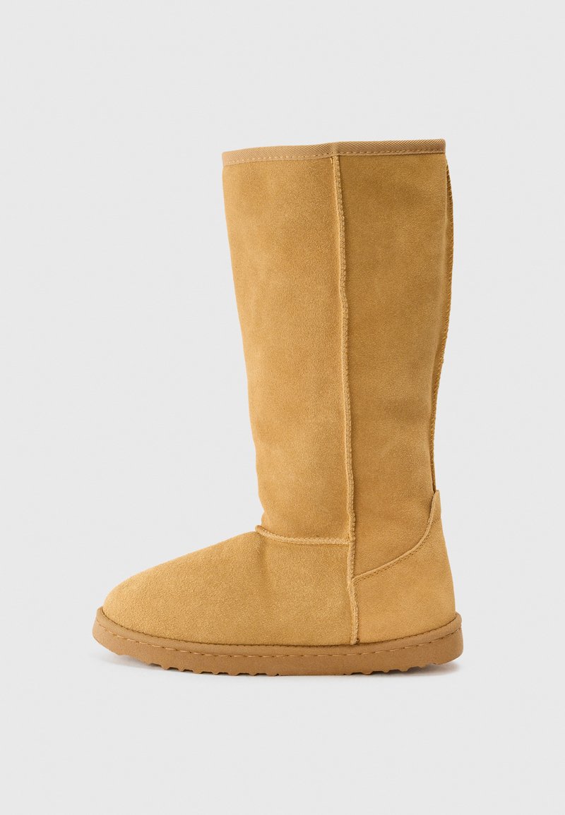 Knee-high tan suede boot with a smooth texture, rounded toe, reinforced seams, and a flat rubber sole. Design offers a simple, classic silhouette.