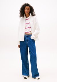Witte fleecejas met hoge kraag, rood en blauw gestreept crop top, wijde blauwe jeans en witte sneakers. Zachte textuur overal.