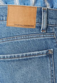 Jeans in denim con lavaggio chiaro, caratterizzati da cuciture arancioni a contrasto, una patch con l'etichetta "7 FOR ALL MANKIND" e un bottone metallico.