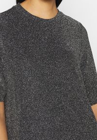 Camiseta de punto negra con manchas, de manga corta y cuello redondo, con una textura suave y un ligero brillo.