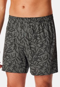 Herren-Badehose mit elastischem Bund, grauem Stoff mit schwarzem Blättermuster und einem Knopf auf der Vorderseite. Weiches, leichtes Material.