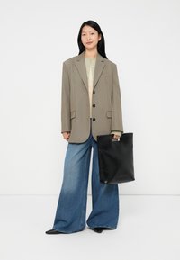 Übergroßer grauer Blazer mit drei Knöpfen, hellgrünes Hemd mit Knöpfen, weit geschnittene blaue Jeans und eine schwarze Tragetasche mit einem Griff.