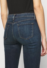 Jeans de mezclilla oscura con un diseño ajustado, cinco bolsillos y detalles de costura mínimos. La cinturilla cuenta con pasadores para el cinturón.