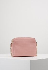 Borsa rettangolare in finta pelle rosa con superficie texture, chiusura con zip e tracolla in catena dorata, posizionata su uno sfondo chiaro.