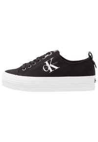Baskets en toile noire avec une semelle en caoutchouc blanche, dotées de lacets, d'une languette de tirage à l'arrière et d'un logo Calvin Klein blanc bien en évidence sur le côté.