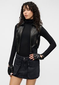 Črna usnjena prilegajoča se kratka jopica čez oprijet črn puli, združena z visokim pasom temno denim mini krila z dvema velikima sprednjima žepoma. Črne rokavice brez prstov.