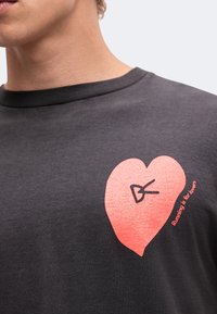 Човек, носещ тъмносива риза с розово сърце и текст "Running is for lovers" на гърдите.