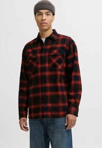 Röd och svart rutigt flanellskjorta med två bröstfickor, knappstängning och svarta knappar. Bärs med blå jeans och en grå undertröja.