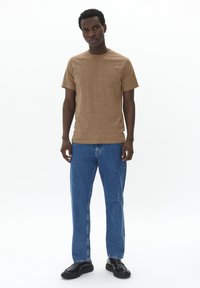 Brown cotton t-shirt with short sleeves, paired with blue denim jeans and black shoes, standing against a white background.