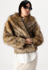 Bruine nep bont cropped jas met een sjawl-collier, een gladde textuur en lange mouwen, gedragen met een wit shirt eronder.