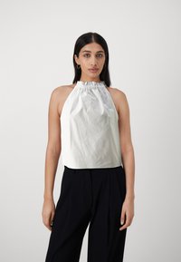 Bílé bezramínkové halter top s nařaseným výstřihem, který má hladkou strukturu. V kombinaci s černými kalhotami s vysokým pasem. Jednoduchý design.