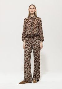 Bluse und Hose mit Tierdruck in Braun und Beige, mit einem Bindedetail am Hals und weitem Bein. Wildlederschuhe ergänzen das Outfit.