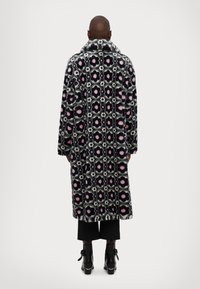 Cappotto in pelliccia sintetica con motivo floreale in rosa, nero e bianco. Dotato di un ampio colletto e maniche lunghe, che termina sotto le ginocchia.