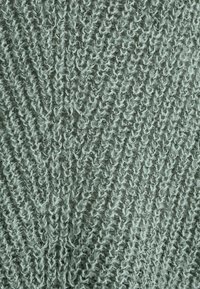 Jasnozielona dzianina z teksturowanym, skośnym wzorem, z widocznymi pętlami i miękkim, puszystym wyglądem.