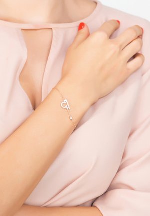 Gold-toned bracelet featuring a key design with small clear gems, attached to a delicate chain, worn on a light-skinned wrist.