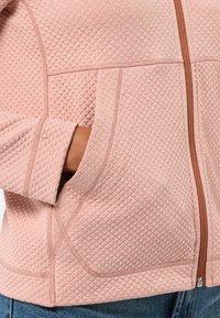 Giacca imbottita rosa con un motivo texturizzato, dotata di una cerniera marrone e tasche laterali. Il materiale sembra morbido e leggermente elastico.
