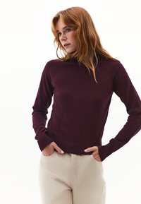Bordeaux coltrui met aansluitende pasvorm, met geribde manchetten en zoom, een strakke textuur, gecombineerd met beige broeken. Eenvoudig, klassiek ontwerp.