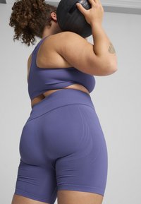 Sportivo reggiseno atletico viola e pantaloni corti a vita alta realizzati in materiale elastico, con dettagli delle cuciture curve e una superficie liscia.