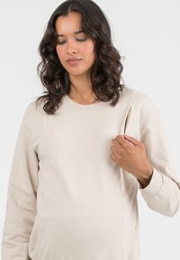 Felpa beige a maniche lunghe in tessuto morbido, con colletto a girocollo e accenti nei pannelli laterali. Tessurizzata, con una vestibilità comoda.