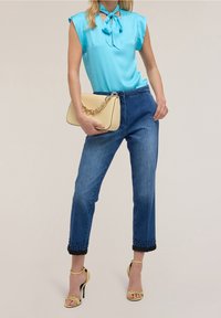 Light blue satin blouse with a tie neckline, paired with high-waisted blue denim jeans featuring black crochet trim at the cuffs. Yellow handbag and heels.