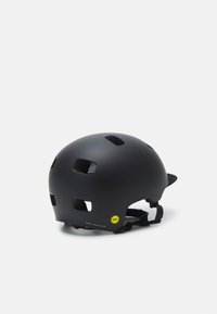 Casco da ciclismo nero realizzato in plastica opaca, dotato di fori di ventilazione, cinturini regolabili e un adesivo giallo MIPS sul lato.