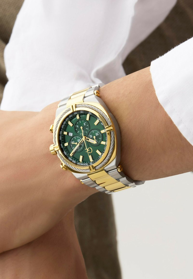Kronografklocka med grön urtavla, guldindex, band av rostfritt stål i silver och guldton, samt strukturerade detaljer på bezeln.