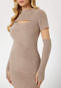 Femme portant une robe en tricot beige duveteux à manches courtes, avec une découpe sur la poitrine et des gants longs assortis sans doigts.