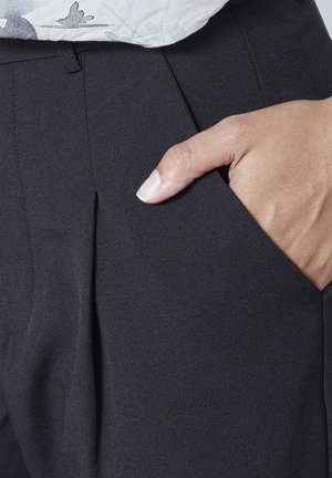 Sorte skræddersyede bukser med et glat, tekstureret stof. Har en frontlomme og skarpe pressede folder, der fremhæver et strømlinet udseende.