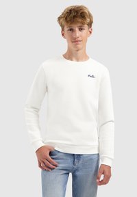 Witte sweatshirt van zachte stof met lange mouwen, ronde hals en een klein geborduurd logo op de borst. Gepaard met lichtblauwe jeans.