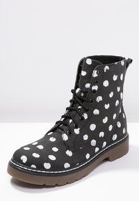 Bottes en toile noire à pois blancs. Le design comprend six œillets, une semelle en caoutchouc, et une empeigne textile avec un bout rond et des accents cousus.