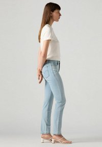 Vaqueros de mezclilla azul claro con corte recto, material de algodón, cintura de altura media, combinados con una camiseta blanca de manga corta y sandalias con tira.
