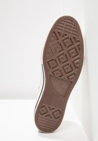 Semelle d'une basket blanche Converse All Star montrant un motif brun sur la bande de roulement et la taille huit visible sur une surface blanche.