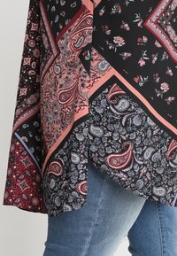 Černá tkanina s květinovými a paisley vzory v červené, modré a fialové. Obsahuje vrstvený design a mírně zaoblený lem.