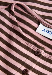 Prim-plan cu material roz și maro cu dungi, cu guler rotund și două nasturi maro lângă guler, afișând o parte dintr-o etichetă albă.