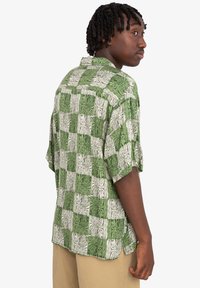 Camisa de manga corta con un patrón de cuadros en verde y blanco, que asemeja la textura de la madera, con un corte relajado y diseño de cuello.
