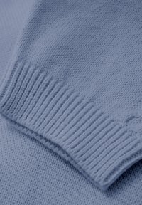 Ljust blått stickat tröjtyg med en ribbad mudd. Mjuk textur och slät mönstring som visar på intrikata söms detaljer.