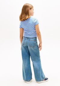 Ριγέ μπλε και λευκό πουκάμισο με κοντά μανίκια, συνδυασμένο με ανοιχτό μπλε τζιν παντελόνι με φαρδιά εφαρμογή. Τα μανίκια και το τελείωμα είναι ξεφτισμένα για υφή.