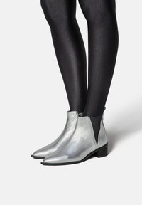Botoși metalici argintii cu vârfuri ascuțite și tocuri mici bloc. Panouri elastice laterale și un finisaj lucios completează designul elegant.