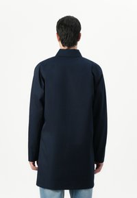 Casaco azul marinho de manga longa com colarinho, corte reto e design minimalista, feito de tecido resistente, com comprimento até metade da coxa.